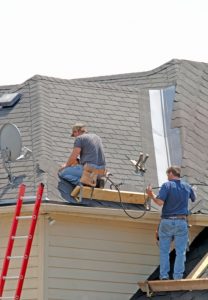 A pair of roofers wearing jeans are applying shingles to a home's roof.