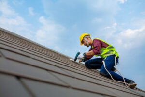 A roofer works on repairing a residential roofing system on a clear day
