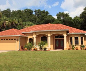 Exterior of single-family home with lush front lawn, peach exterior paint, and red Spanish-style tile roofing.